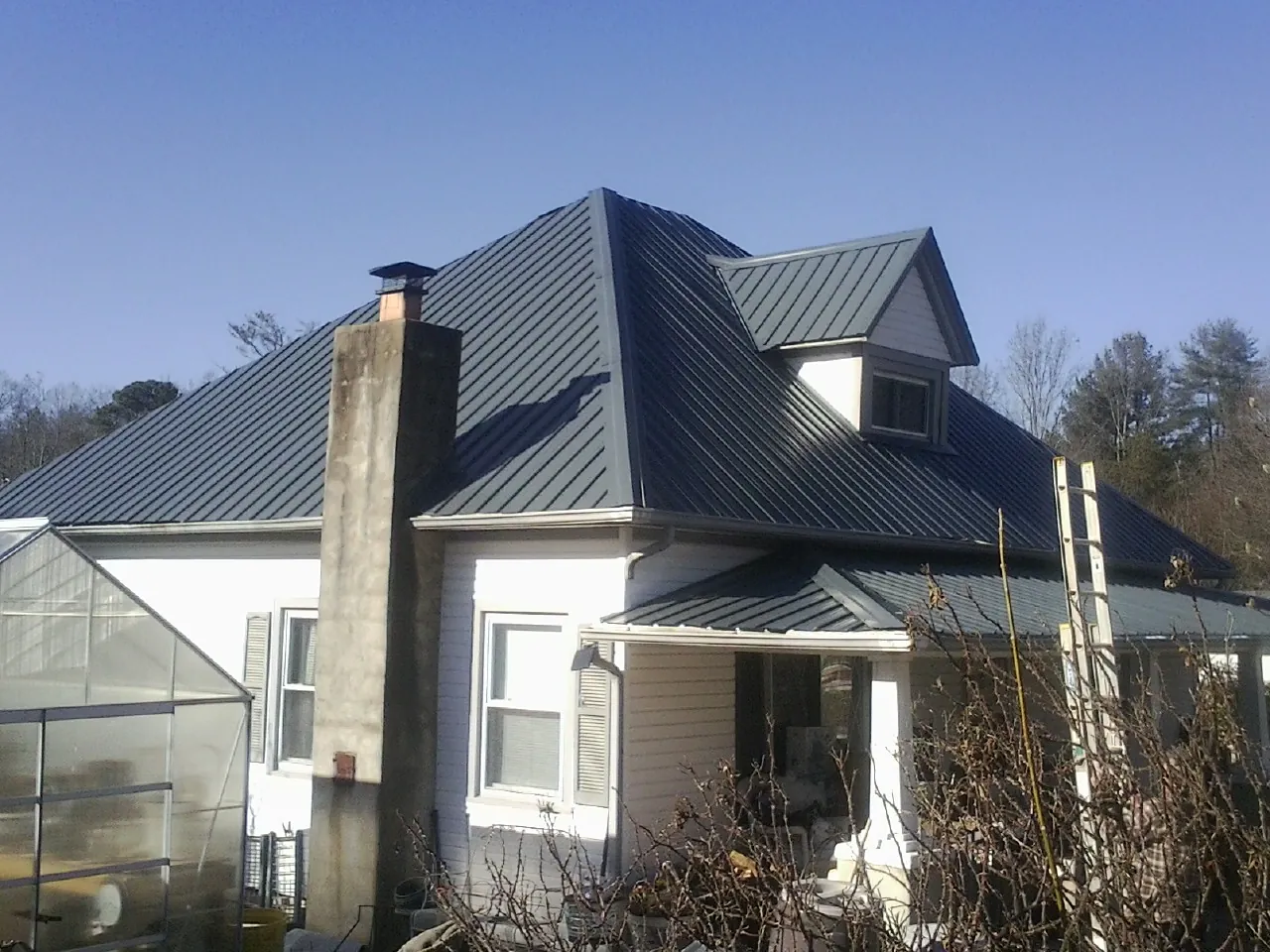Dark blue standing seam metal roof on a white farmhouse with dormer — Slate & Tile Roof Repair by Roofing Brothers in Clarkson