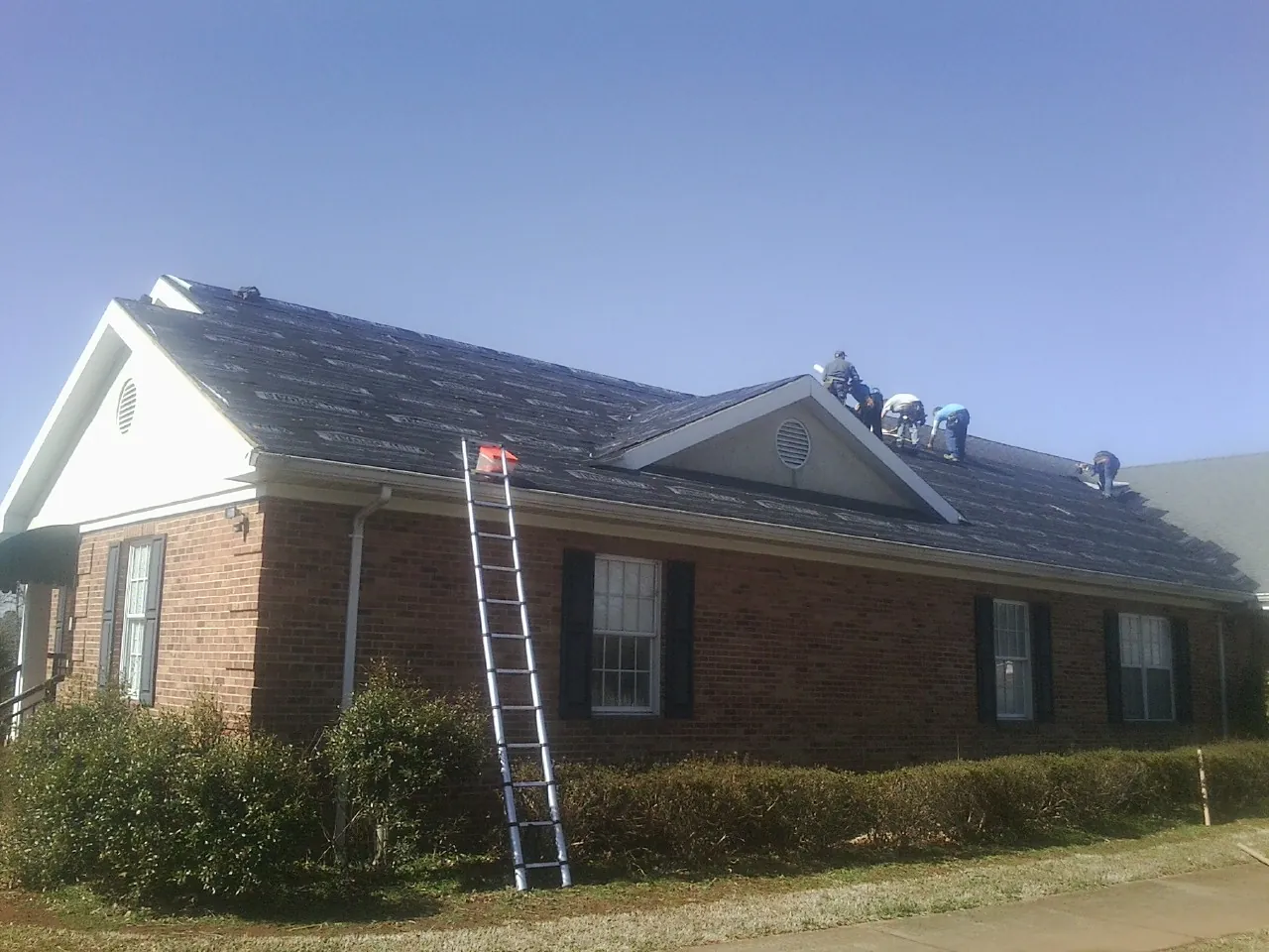 Crew tearing shingles off a brick ranch roof with a ladder set — Emergency Roof Repair work by our crew in Clarkson