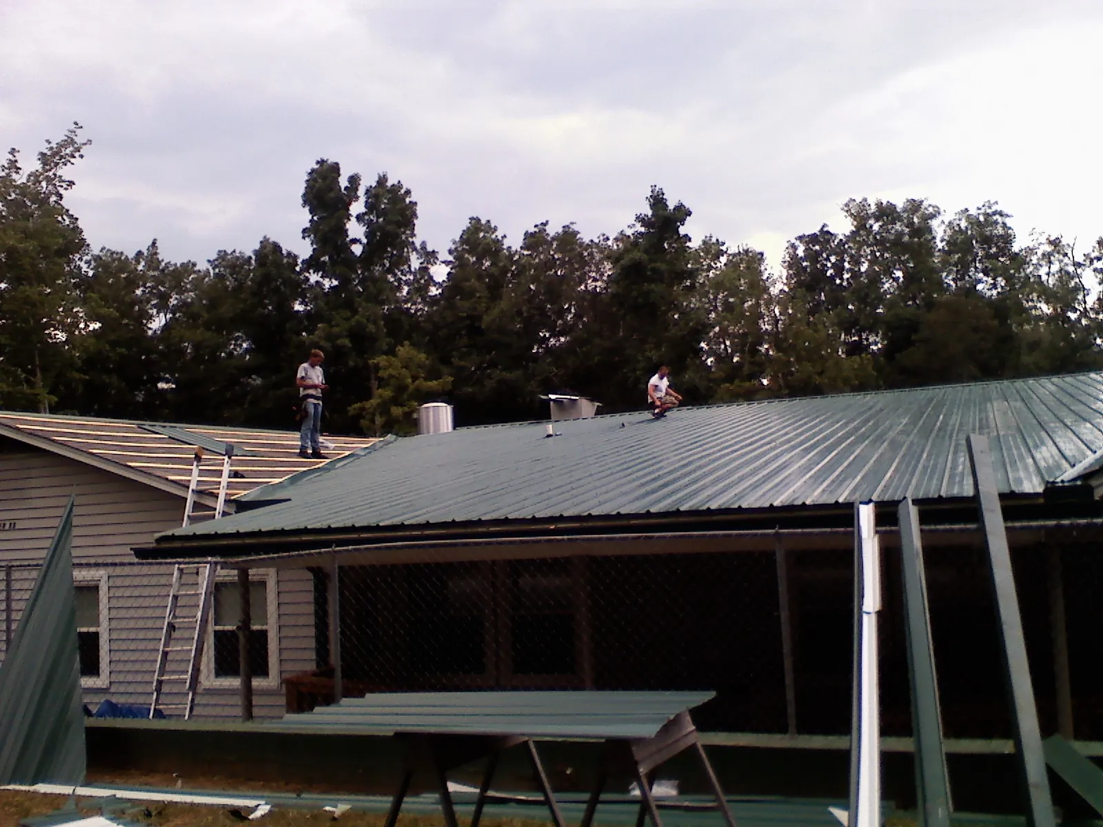 Two roofers installing green metal panels above a covered porch in Clarkson